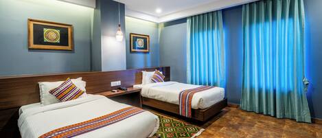A hotel room with two beds, a nightstand, a lamp, and a window with curtains.