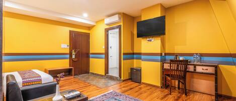 Habitación de hotel con cama, escritorio, silla, televisor y aire acondicionado.
