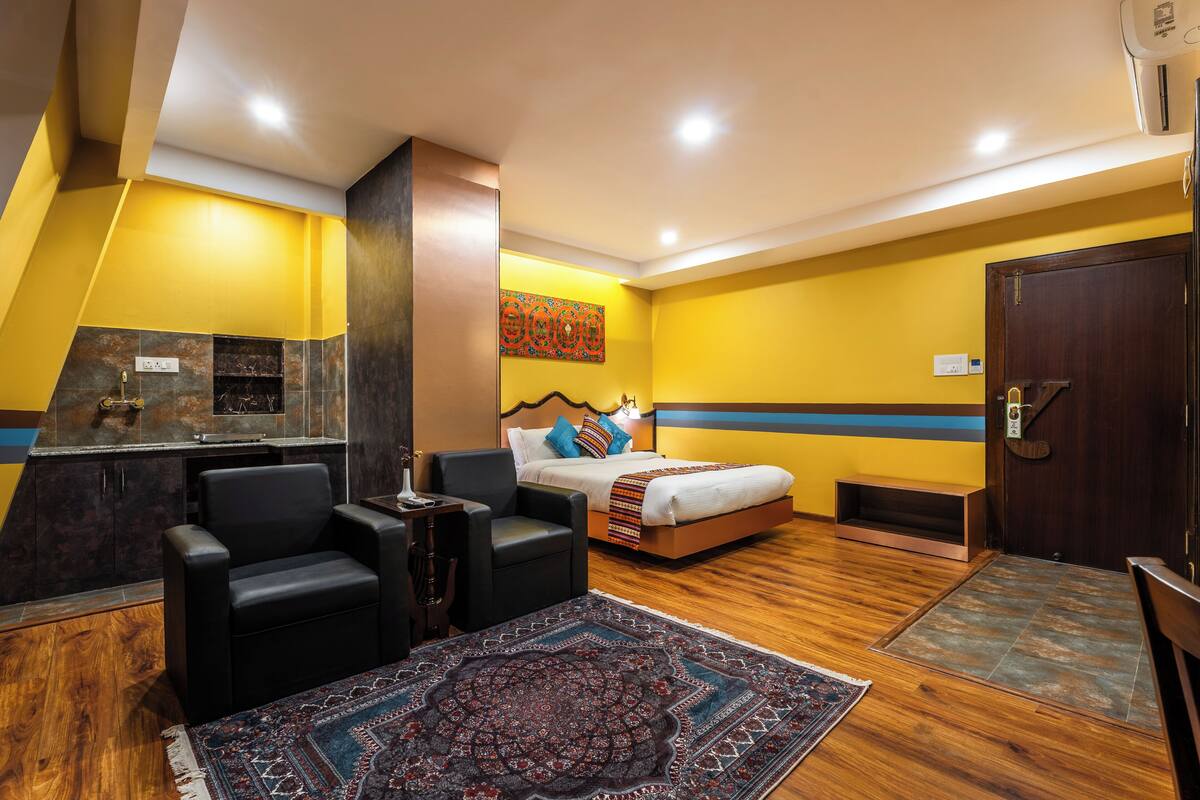 A hotel room with a bed, a desk, a chair, a rug, and a wooden floor.