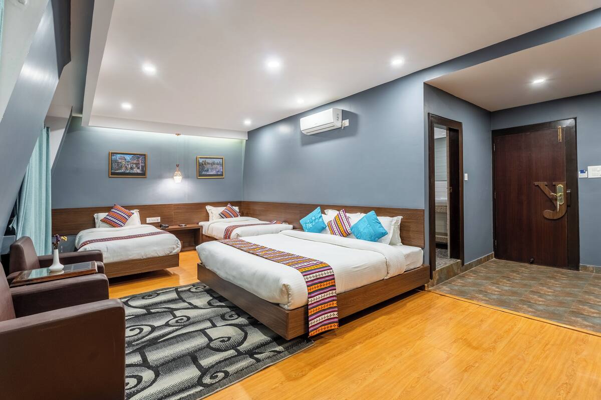 A hotel room with two beds, a sofa, a patterned rug, and an air conditioning unit.