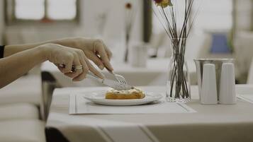 Una persona cortando un pastel sobre un plato blanco, en una mesa con un jarrón de flores secas y saleros.