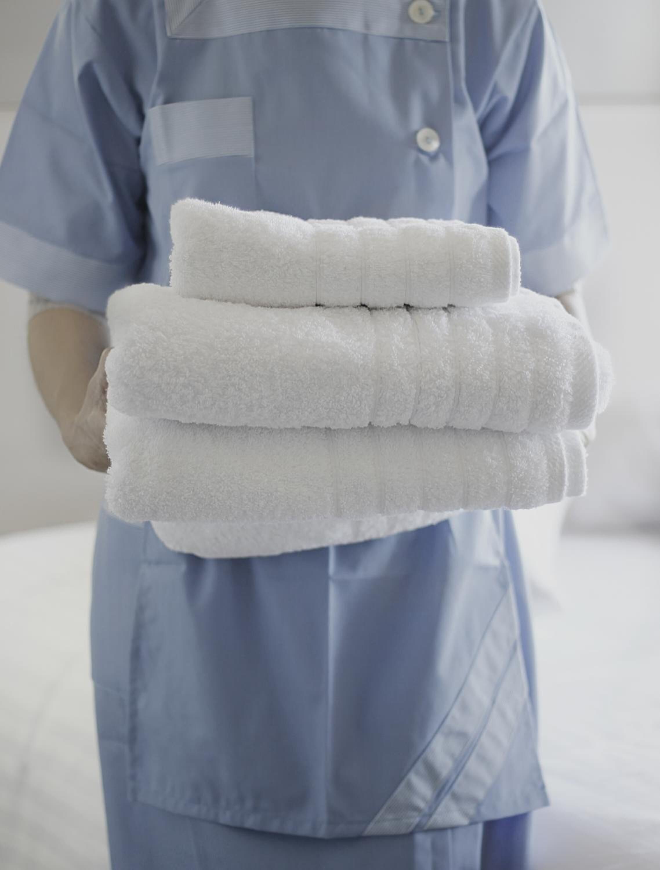 A person in a blue uniform holding a stack of white towels.