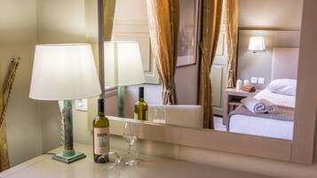 A hotel room with a bed, a bedside table with a lamp, a bottle of wine, and a glass.