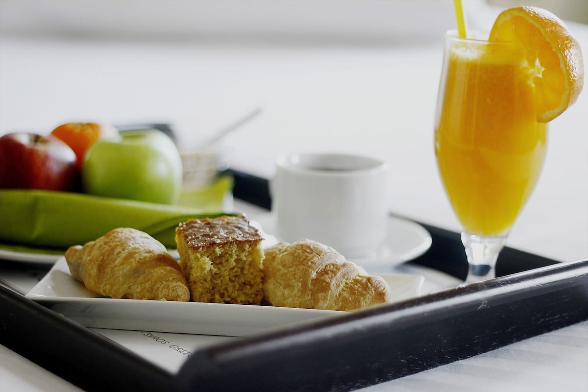 Uma bandeja com croissants, um copo de suco de laranja e uma travessa de frutas.