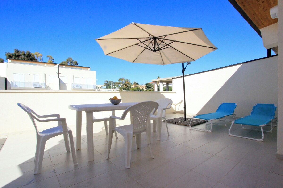 Eine Terrasse mit Tisch, Stühlen, Sonnenschirm und Liegestühlen.