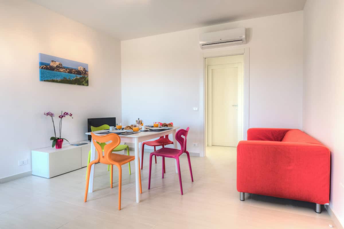 A modern living room with a dining area, a red sofa, and a painting on the wall.