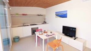 A compact kitchen with white cabinets, a dining table with chairs, a TV, and a small trash bin. - Appartamenti Sud Est (Ragusa)