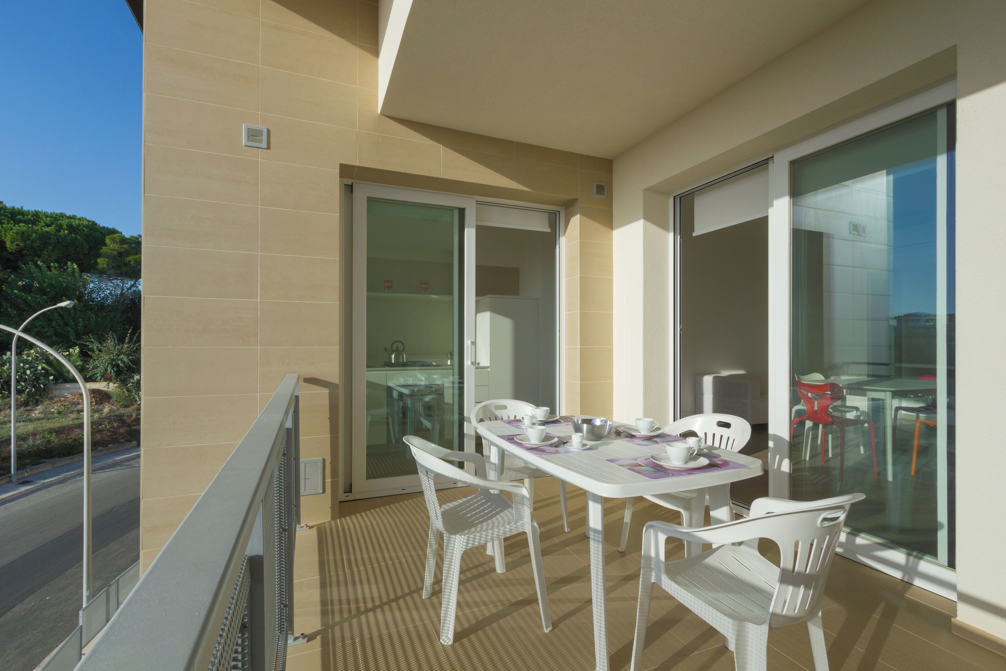 A balcony with a table and chairs, a sliding glass door, and a view of greenery.