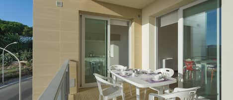 A balcony with a table and chairs, a sliding glass door, and a view of greenery.
