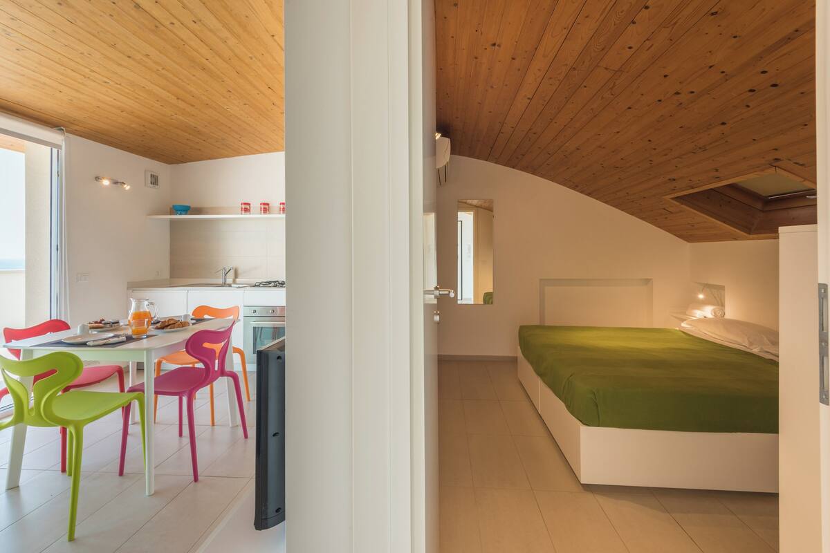 A modern bedroom with a wooden ceiling, a green bed, and a white bedside table.