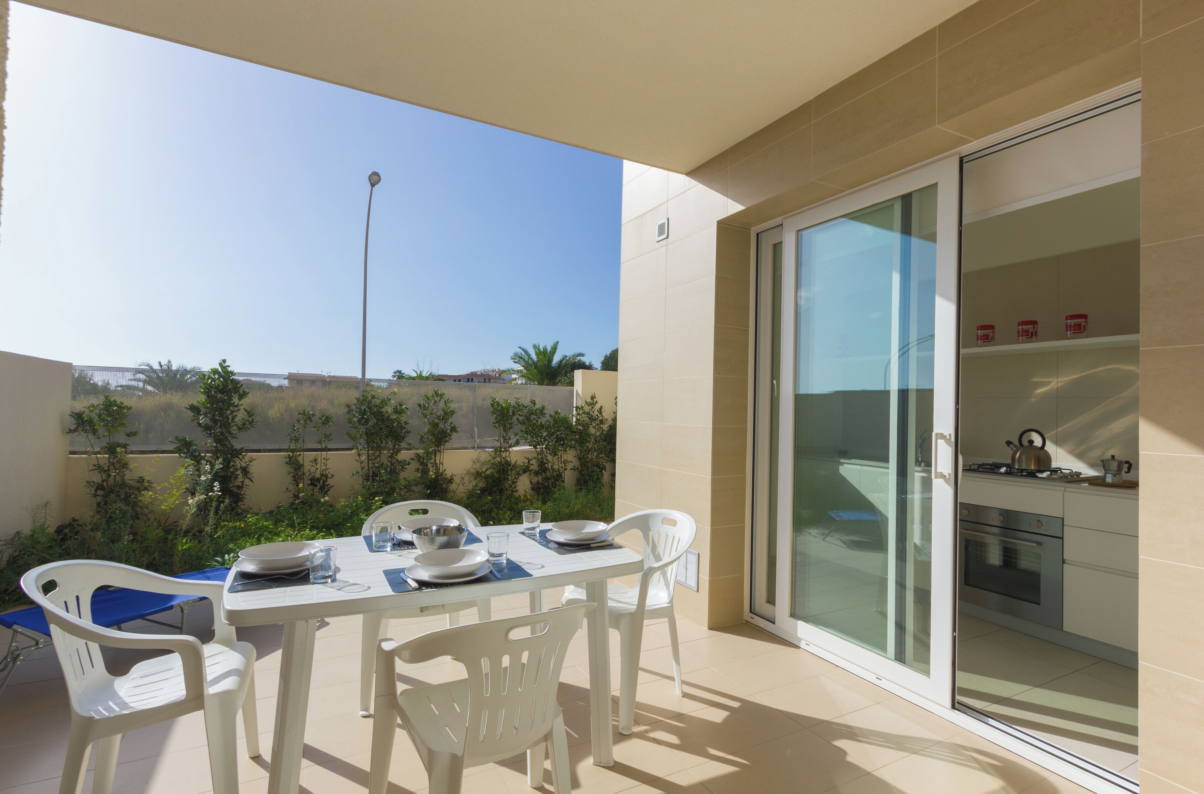 Un balcon avec une table dressée pour les repas, une porte-fenêtre coulissante donnant sur la cuisine et une vue sur les environs.