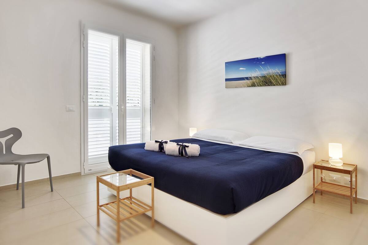 A bedroom with a bed, a nightstand, a chair, and a picture on the wall.