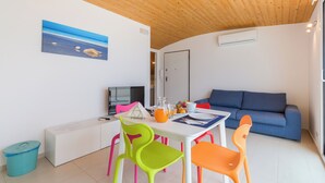 A modern living room with a blue sofa, a dining table with colorful chairs, and a painting of a beach scene on the wall. - Appartamenti Sud Est (Ragusa)