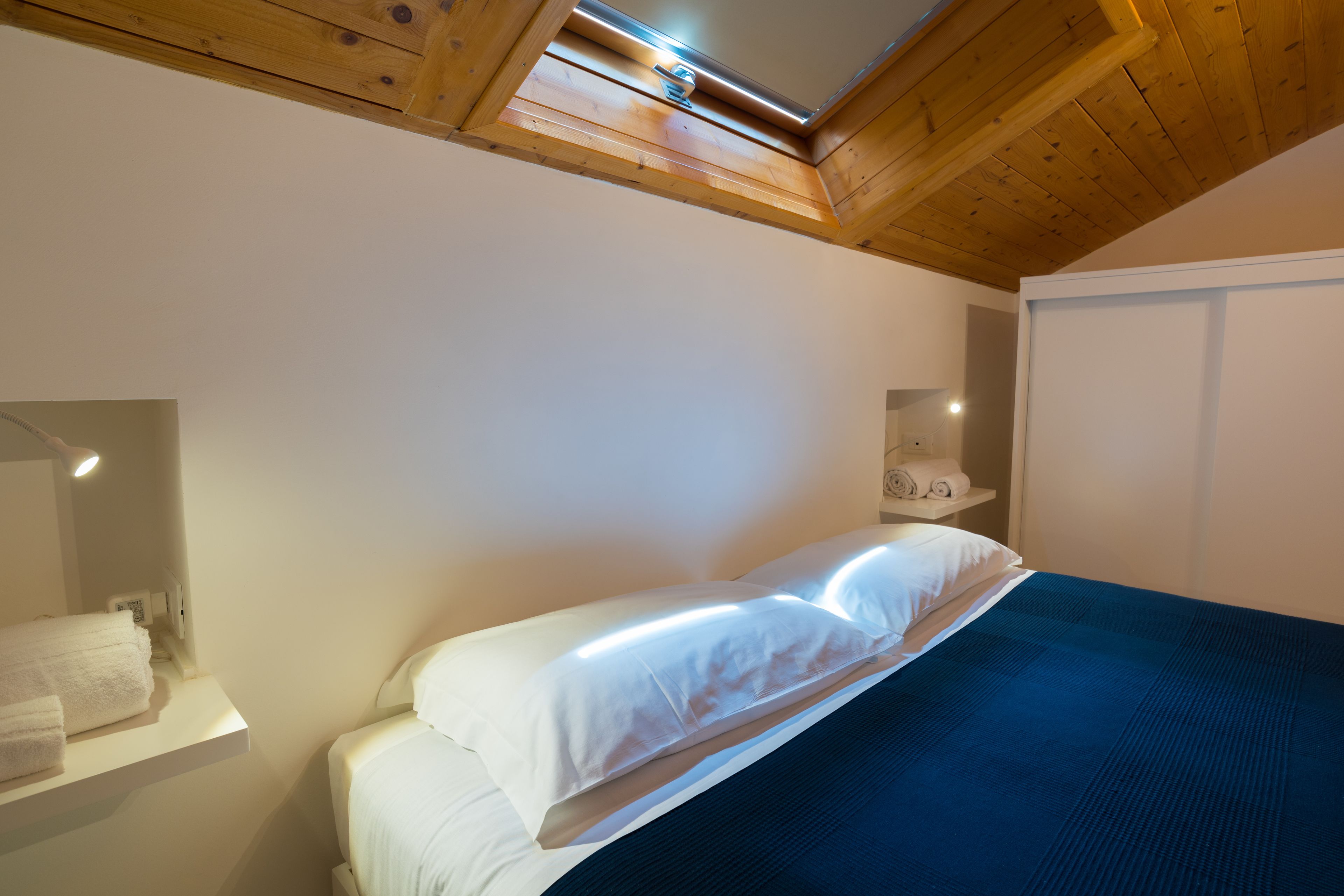 Une chambre à coucher avec un lit, un plafond en bois, un mur blanc, un miroir et un porte-serviettes.