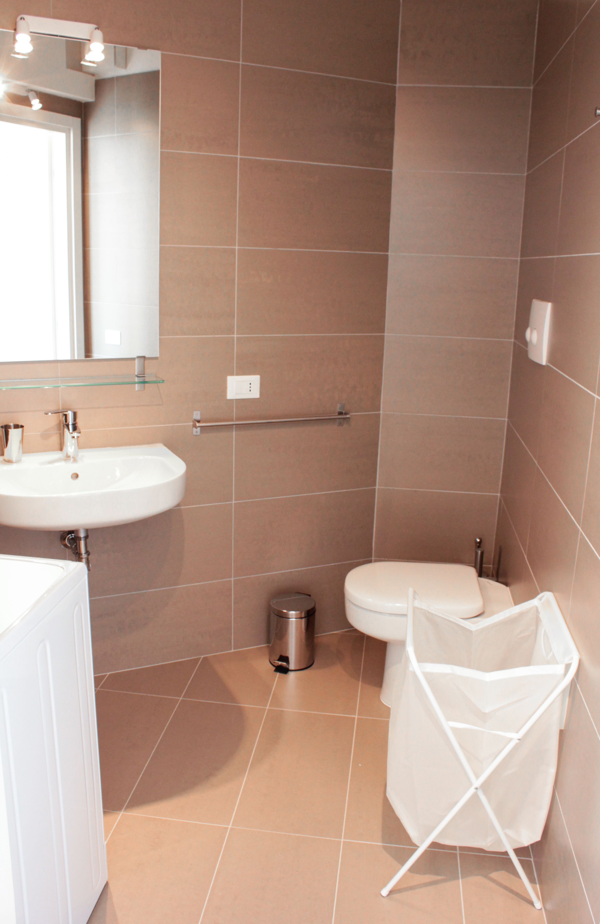 A bathroom with a white sink, a mirror, a toilet, and a trash can.