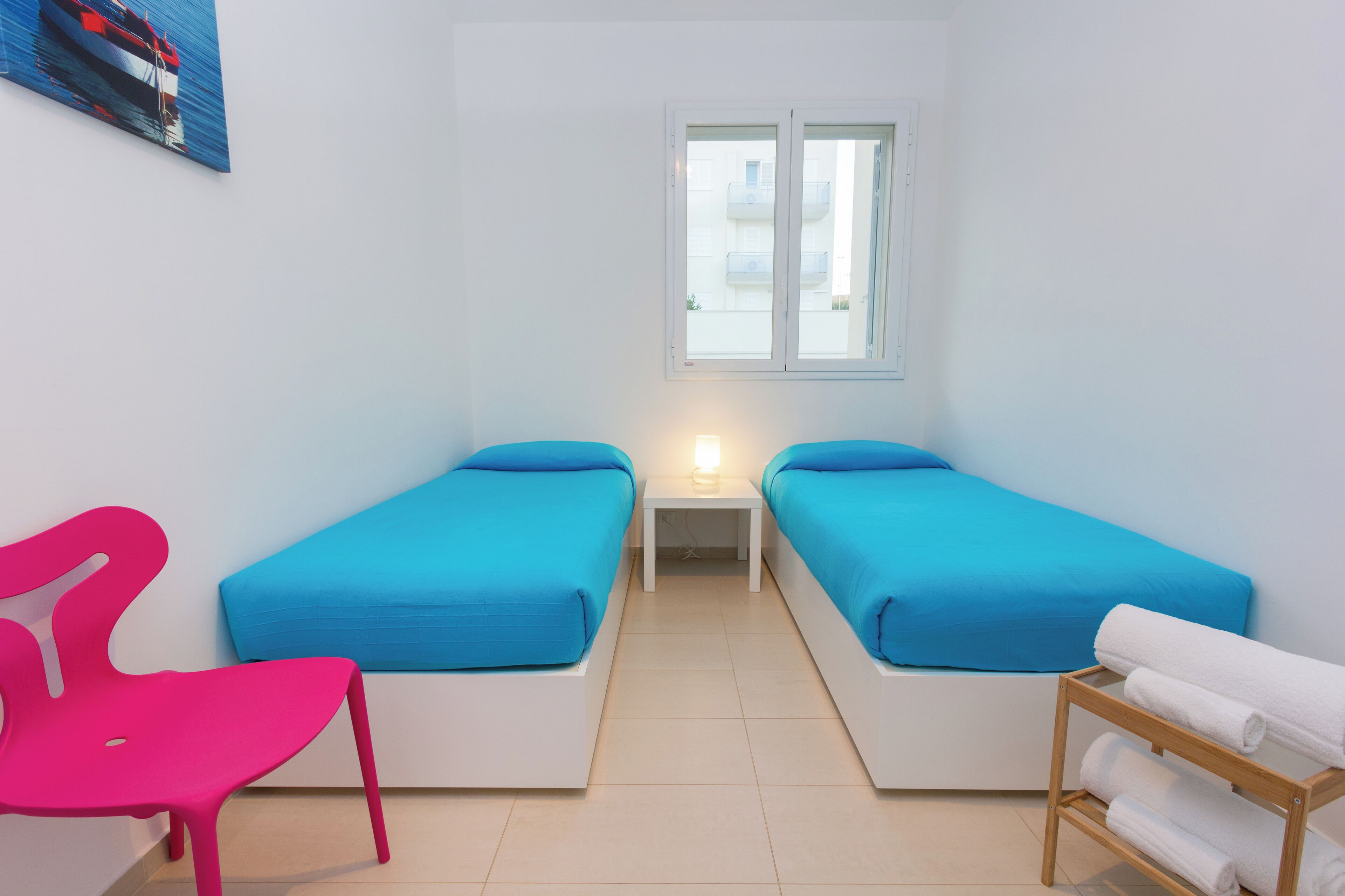 Ein kleines, sauberes Zimmer mit zwei Einzelbetten, einem kleinen Tisch, einem Stuhl und einem Fenster.