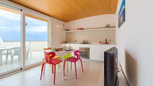 A modern kitchen with a wooden ceiling, a dining area with colorful chairs, and a large window overlooking a balcony. - Appartamenti Sud Est (Ragusa)