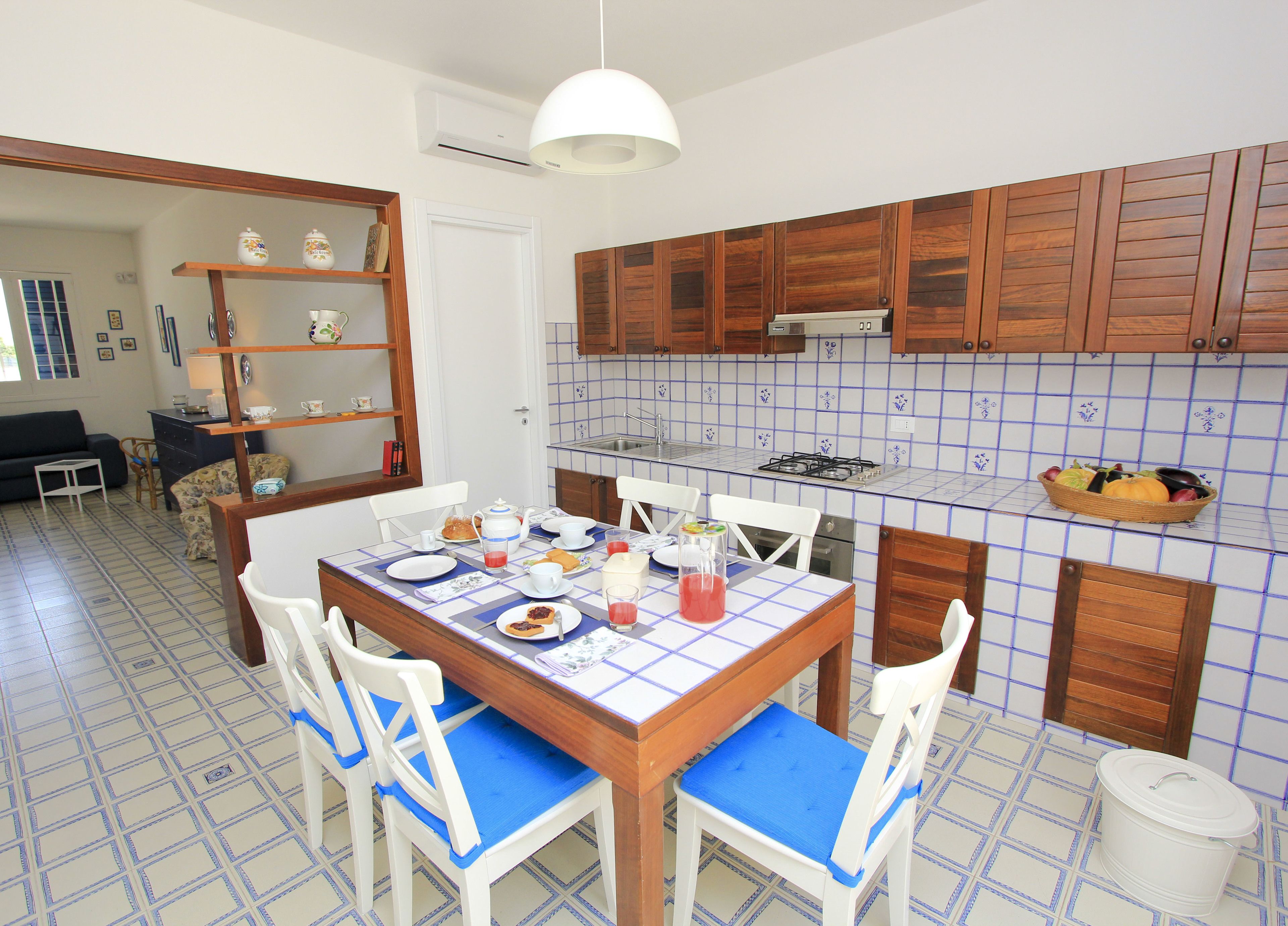 Un coin repas avec une table dressée pour quatre personnes, entouré de chaises blanches dotées de coussins bleus.