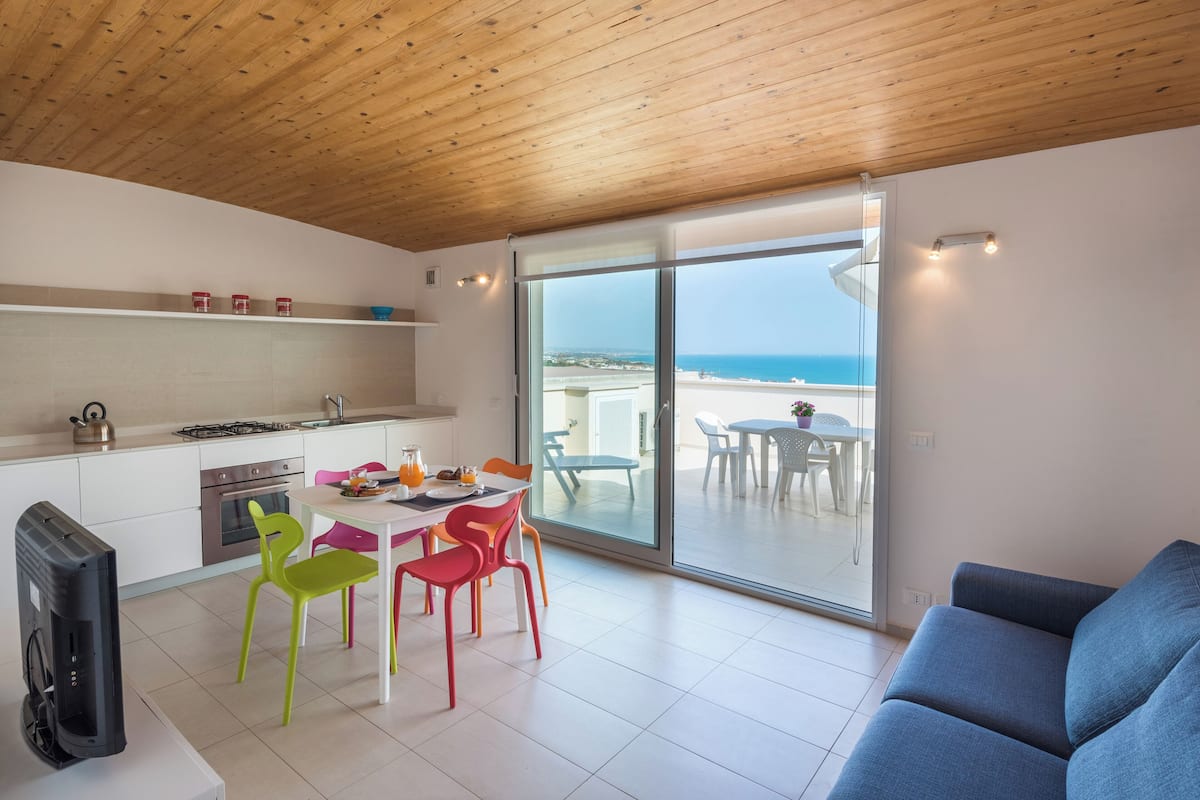 A modern kitchen with white cabinets, a gas stove, and a dining area with colorful chairs.