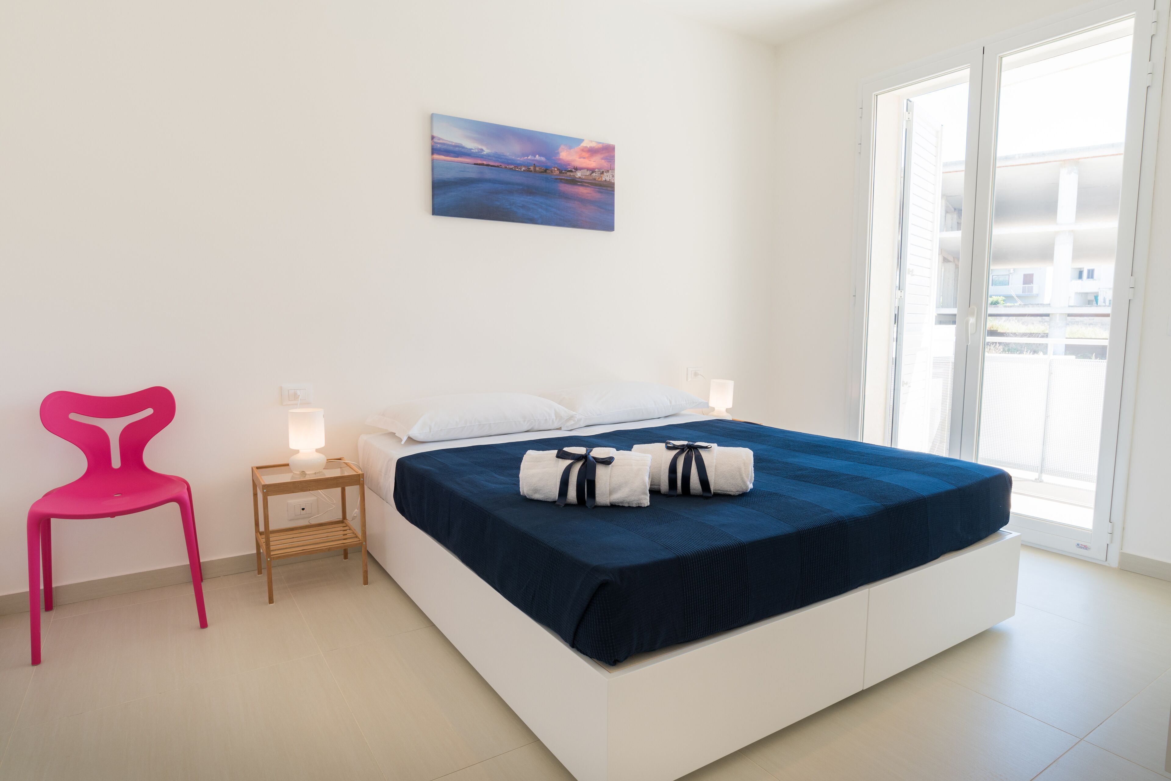 Une chambre à coucher avec un lit, une table de chevet, une lampe, une chaise et une fenêtre donnant sur un beau paysage.