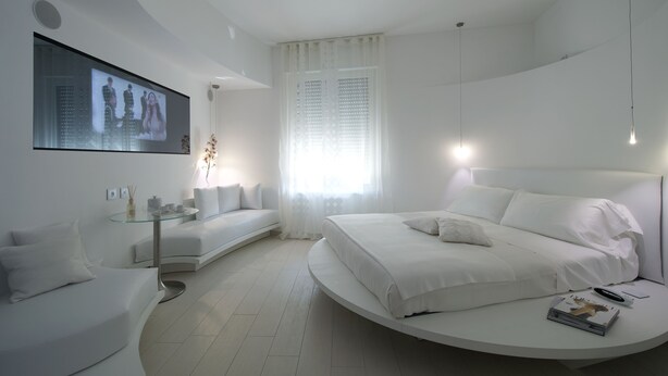 A modern bedroom with a curved bed, a glass coffee table, a sofa, and a TV mounted on the wall. - Aparthotel Duomo (Milan)