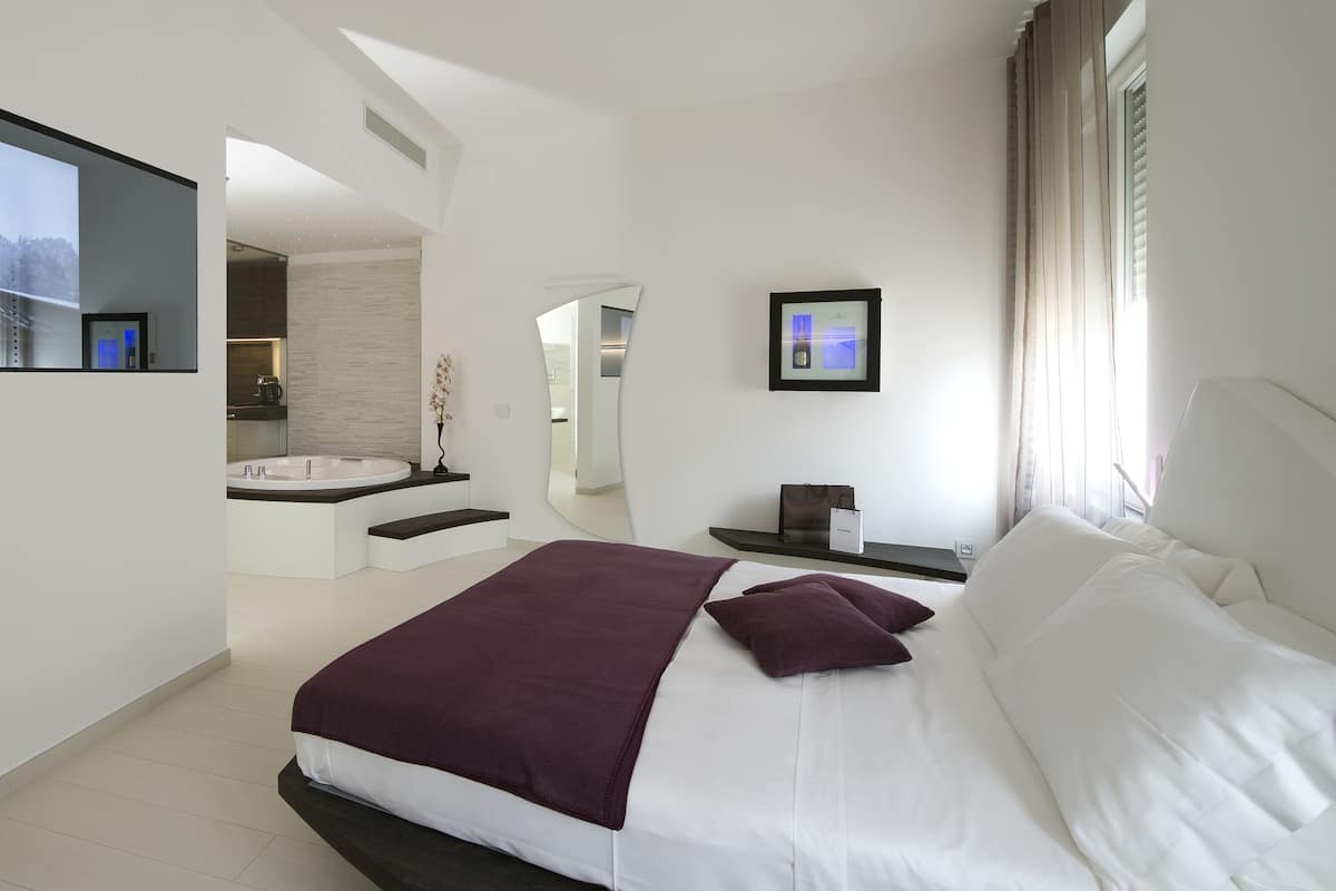 Un hotel moderno con una cama grande, televisión, baño con bañera y vistas a la ciudad.