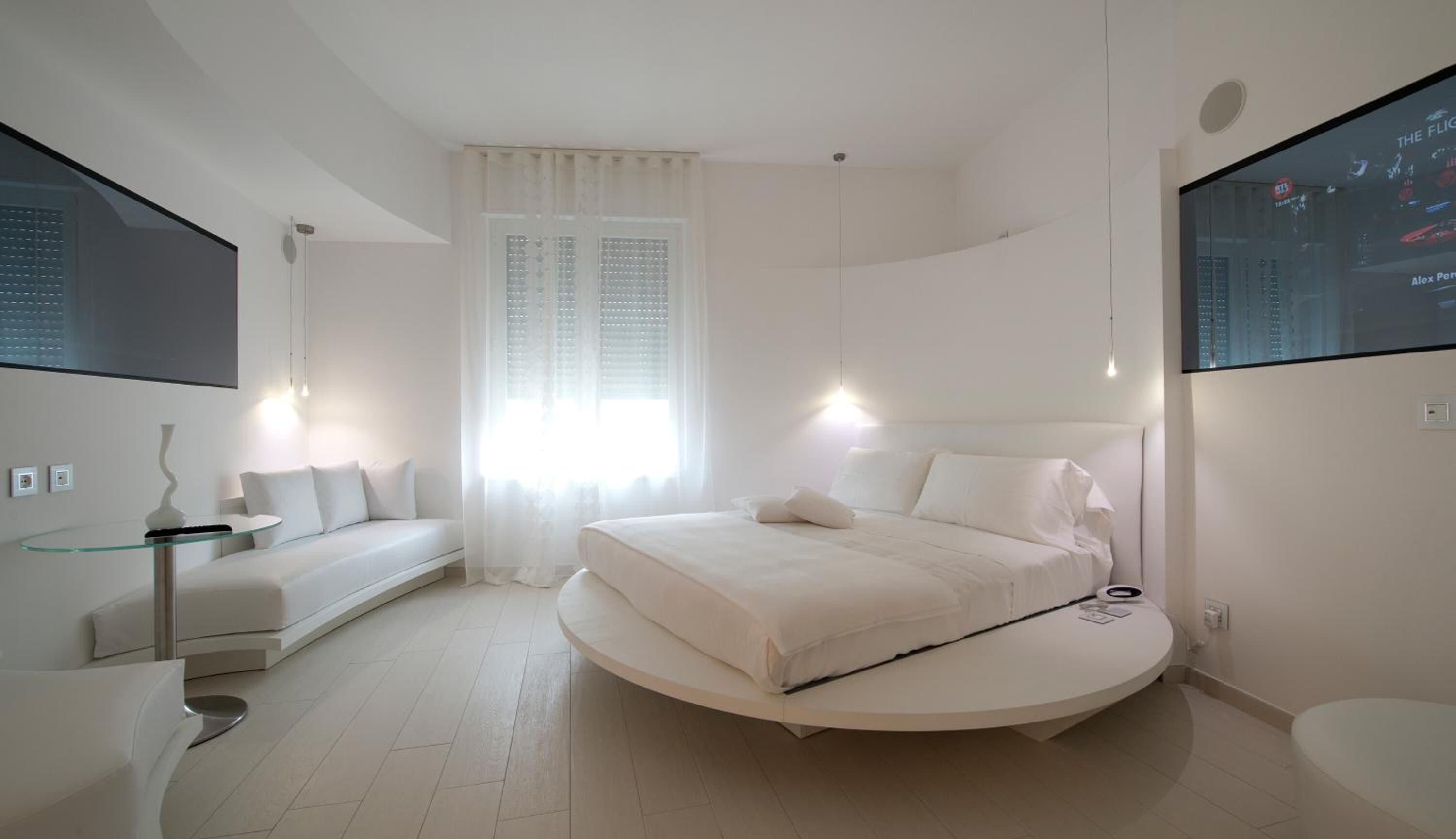 Une chambre moderne avec un lit rond, une table en verre et une grande fenêtre avec des rideaux.