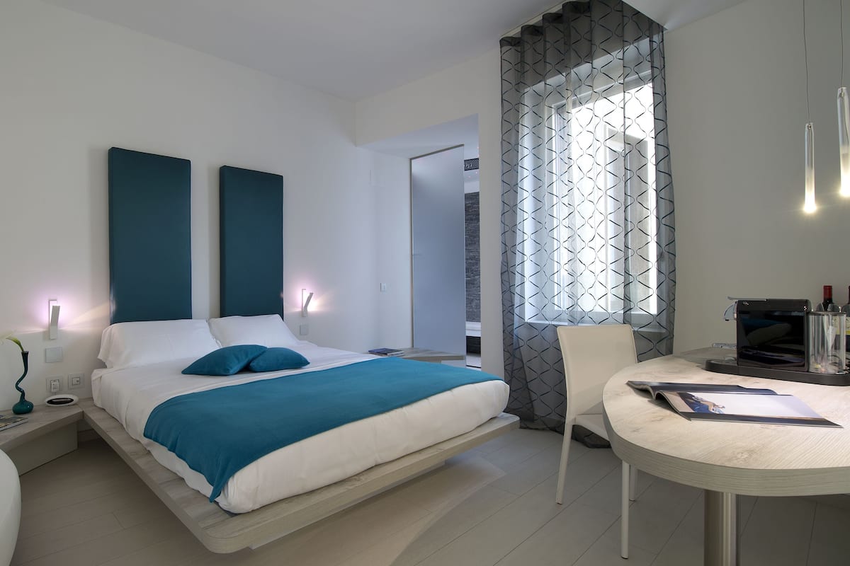 Una habitación de hotel moderna con cama, mesita de noche, silla y una pequeña mesa con una revista.