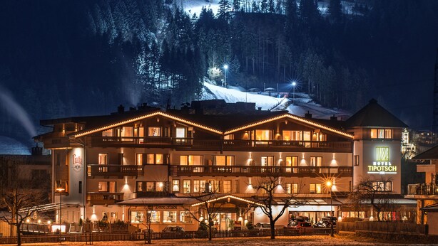 Un grand hôtel à plusieurs étages, reconnaissable à son enseigne imposante, situé au pied d’une montagne enneigée.