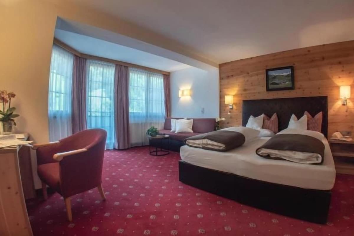 A hotel room with a large bed, a desk, a chair, and a window with curtains.