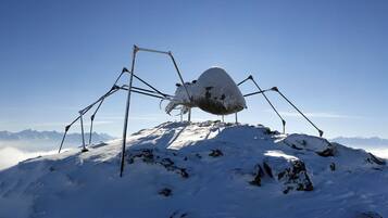 Una vetta montuosa innevata con una grande scultura a forma di ragno al centro.
