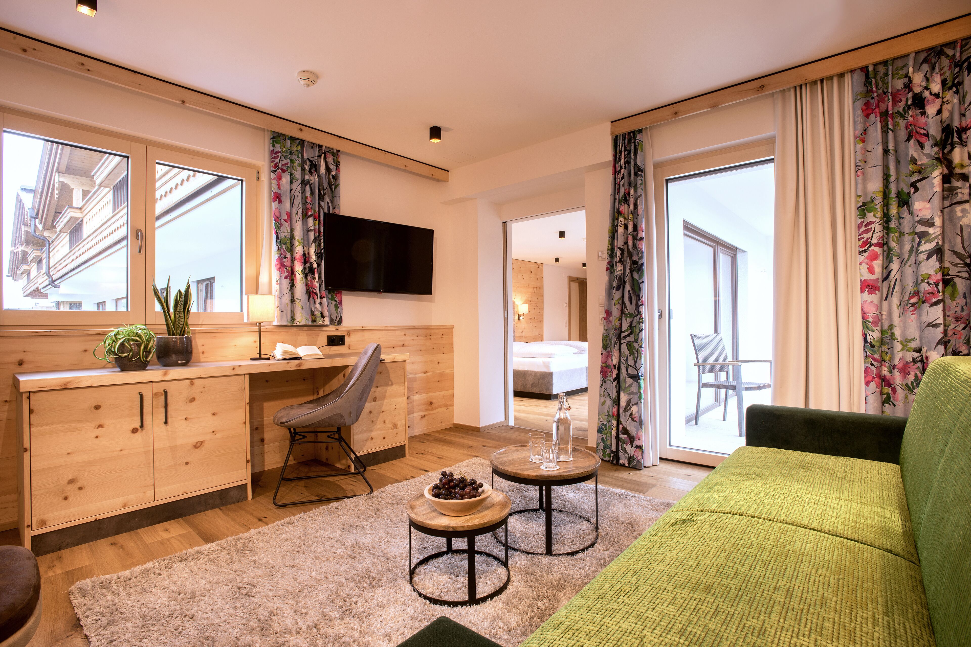 Una sala de estar moderna con un sofá verde, armarios de madera, un televisor de pantalla plana y un comedor con mesa y sillas.