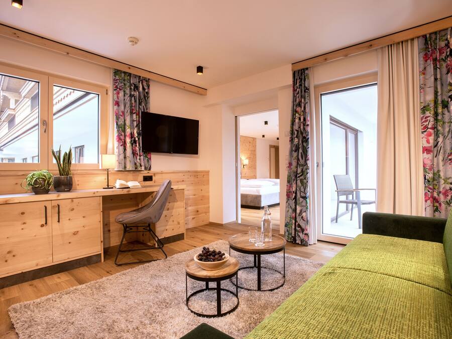 A modern living room with a green sofa, wooden cabinets, a flat-screen TV, and a dining area with a table and chairs.