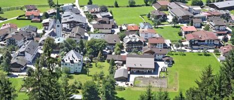 An aerial view of a village with residential buildings, a church, and surrounding green fields.