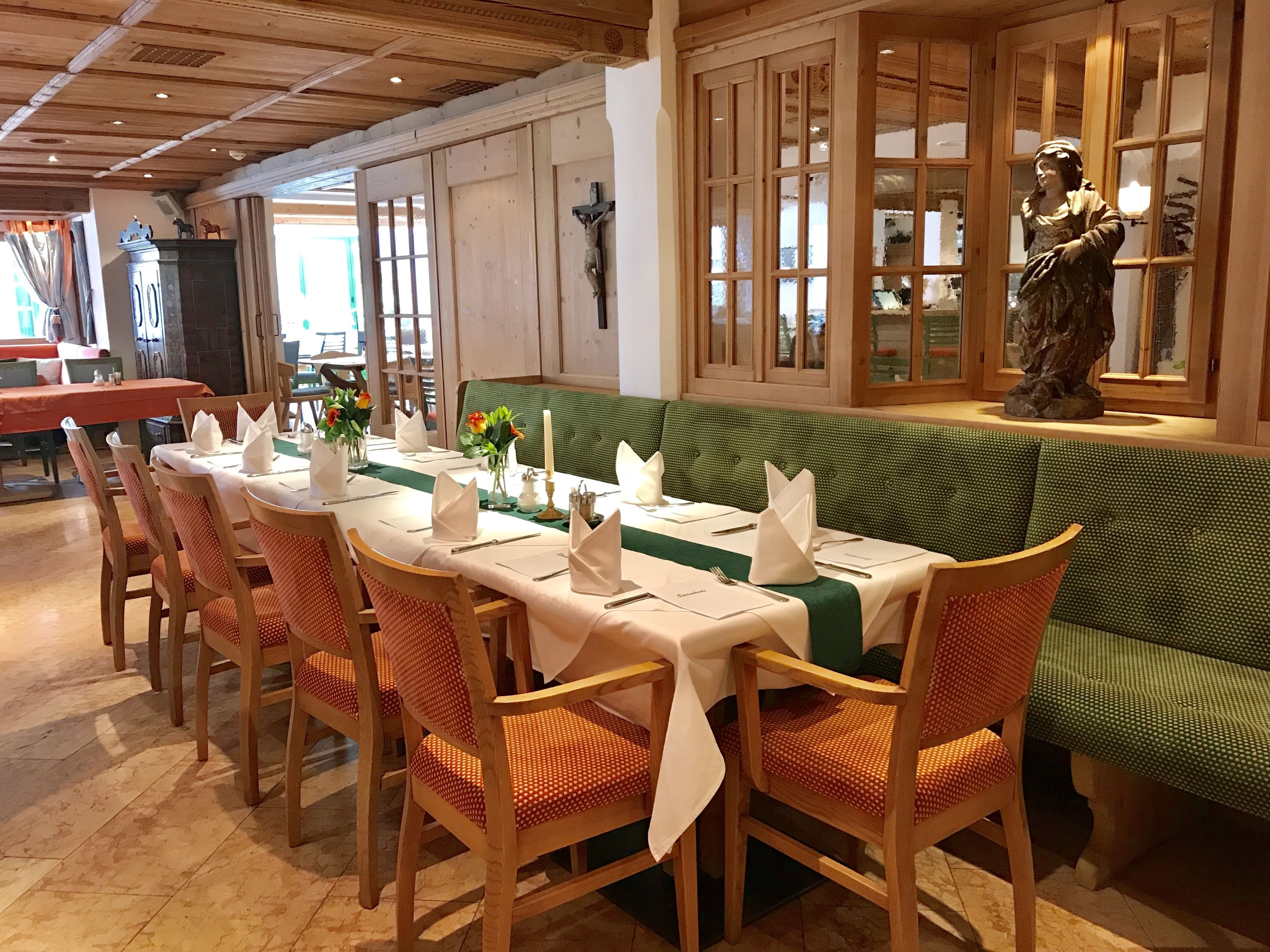 Een eetruimte met een lange tafel gedekt voor een maaltijd, houten stoelen en een groene gestoffeerde bank.