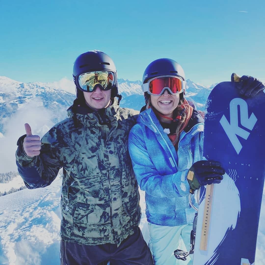 Duas pessoas vestidas para esquiar em uma montanha coberta de neve, com céu claro.