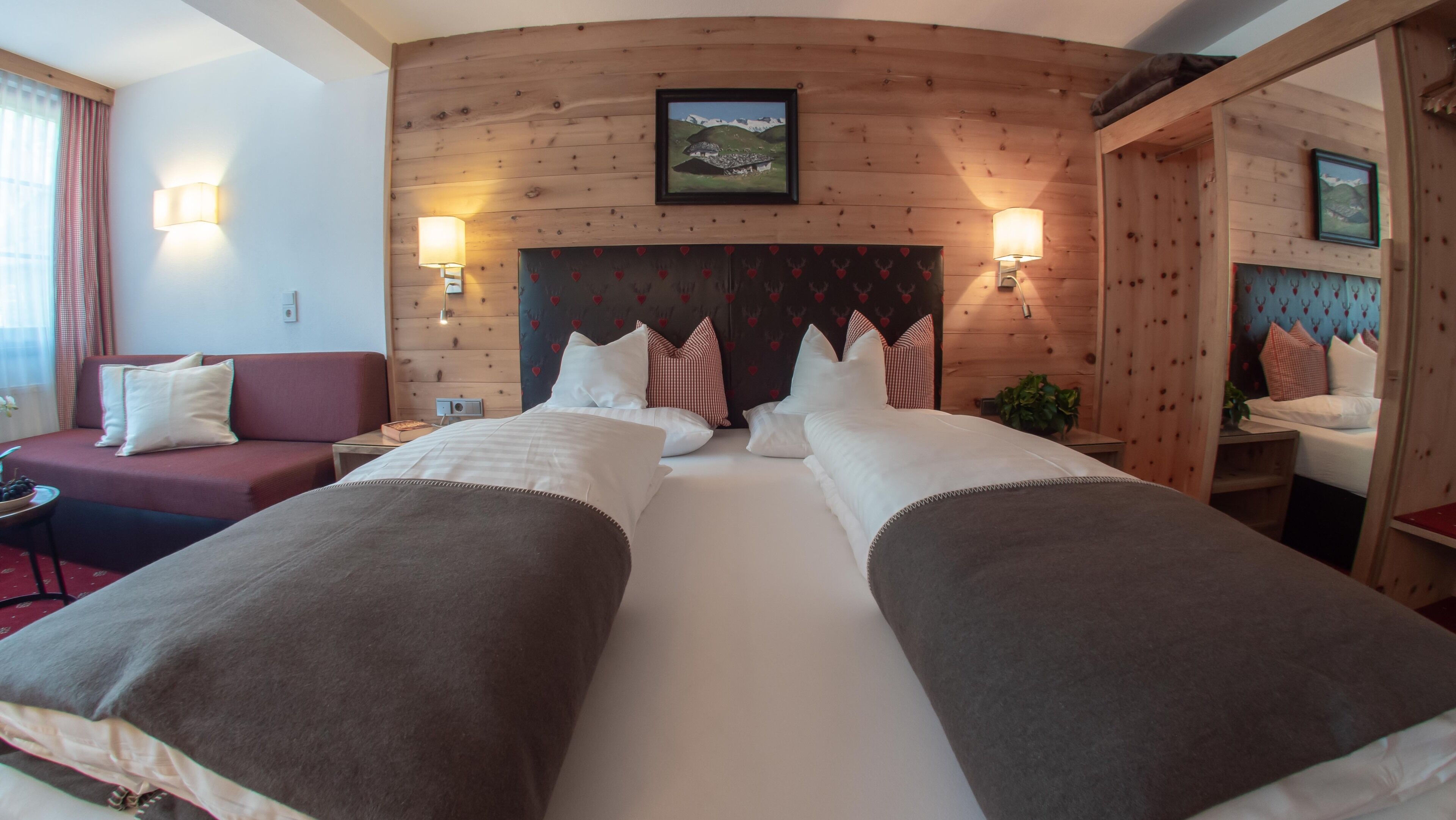 Una cama doble con cabecera de madera, dos mesitas de noche, un sofá rojo y un espejo.