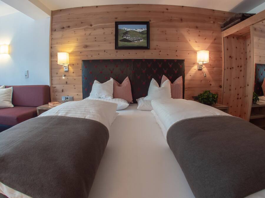 Una cama doble con cabecera de madera, dos mesitas de noche, un sofá rojo y un espejo.