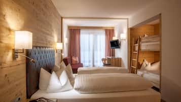 A hotel room with a wooden headboard, a bed with white bedding, a small desk with a chair, a TV mounted on the wall, and a bunk bed with a ladder.