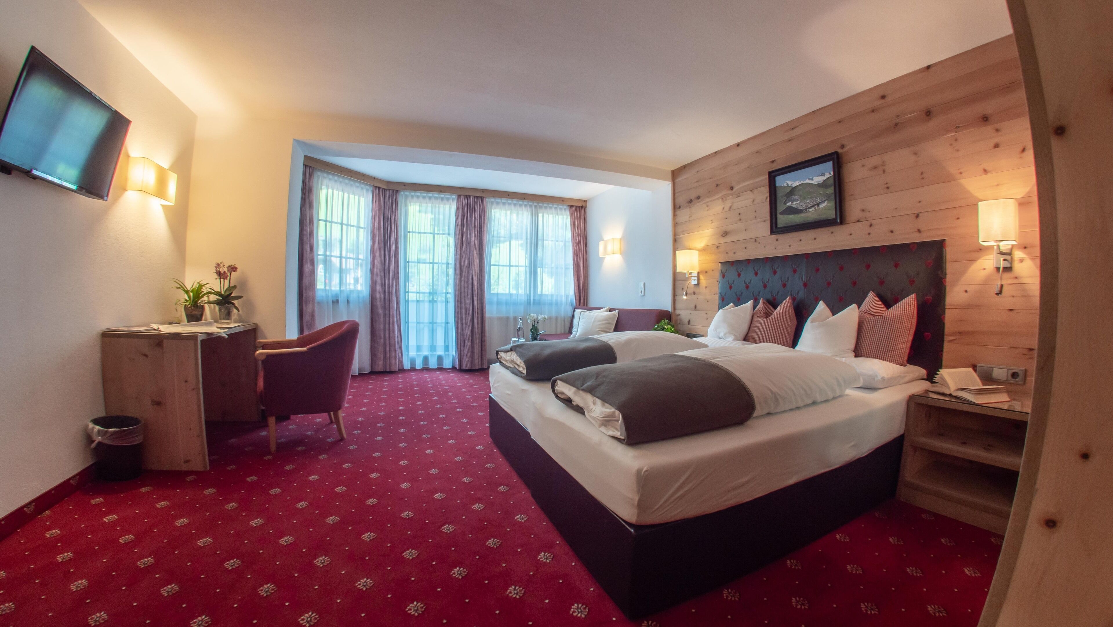 A hotel room with a large bed, a desk, a chair, and a TV on the wall.