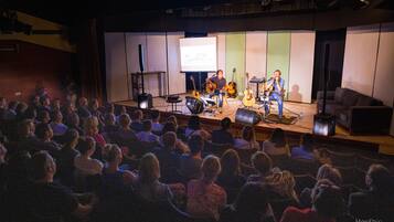 Escenario de concierto con músicos, un público y una pantalla de proyección.