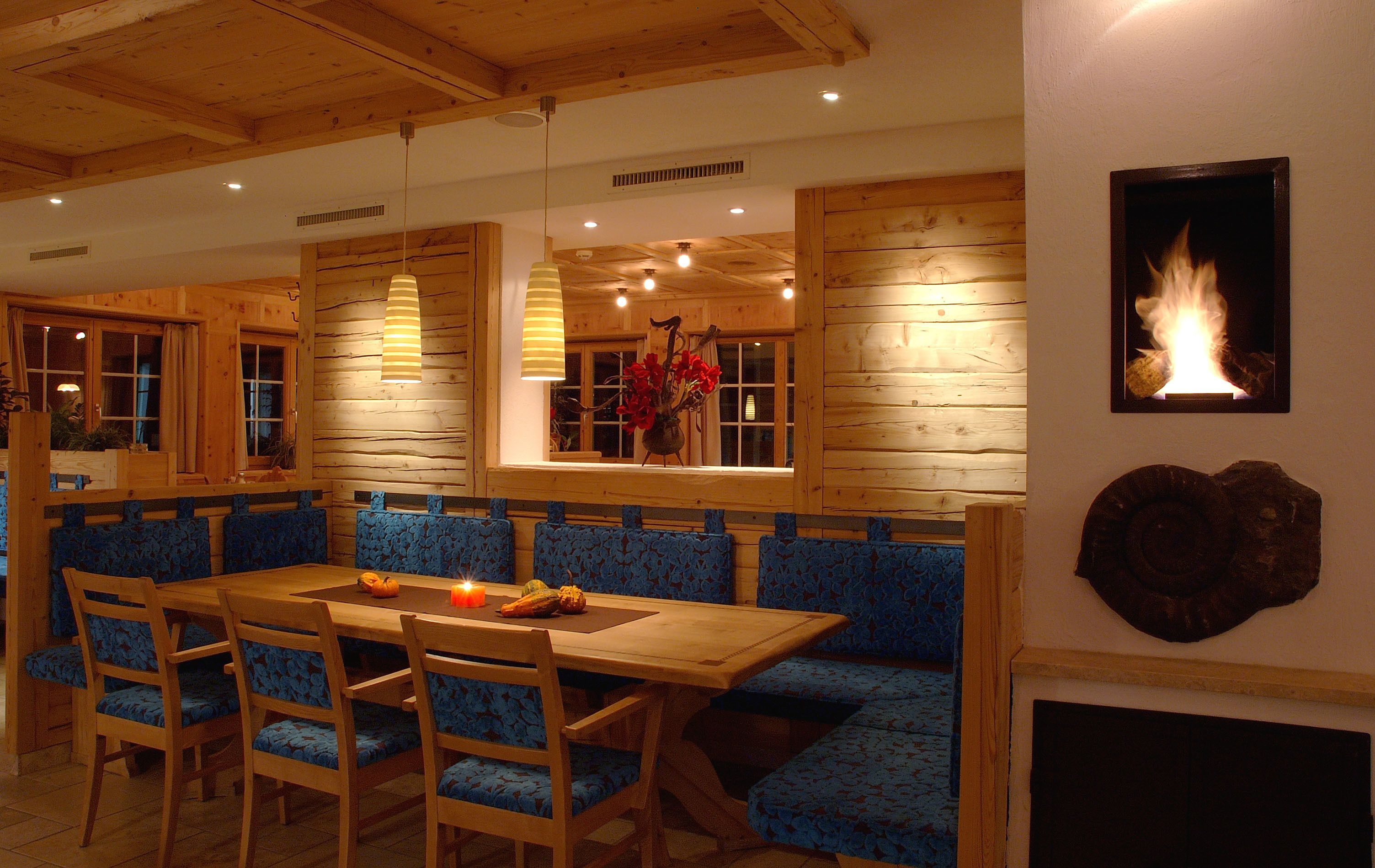 Un comedor con una mesa de madera, bancos tapizados en azul y una chimenea.