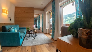 Un salon moderne avec un plancher en bois, un canapé bleu, une table basse et une vue sur un paysage montagneux grâce à de grandes fenêtres.