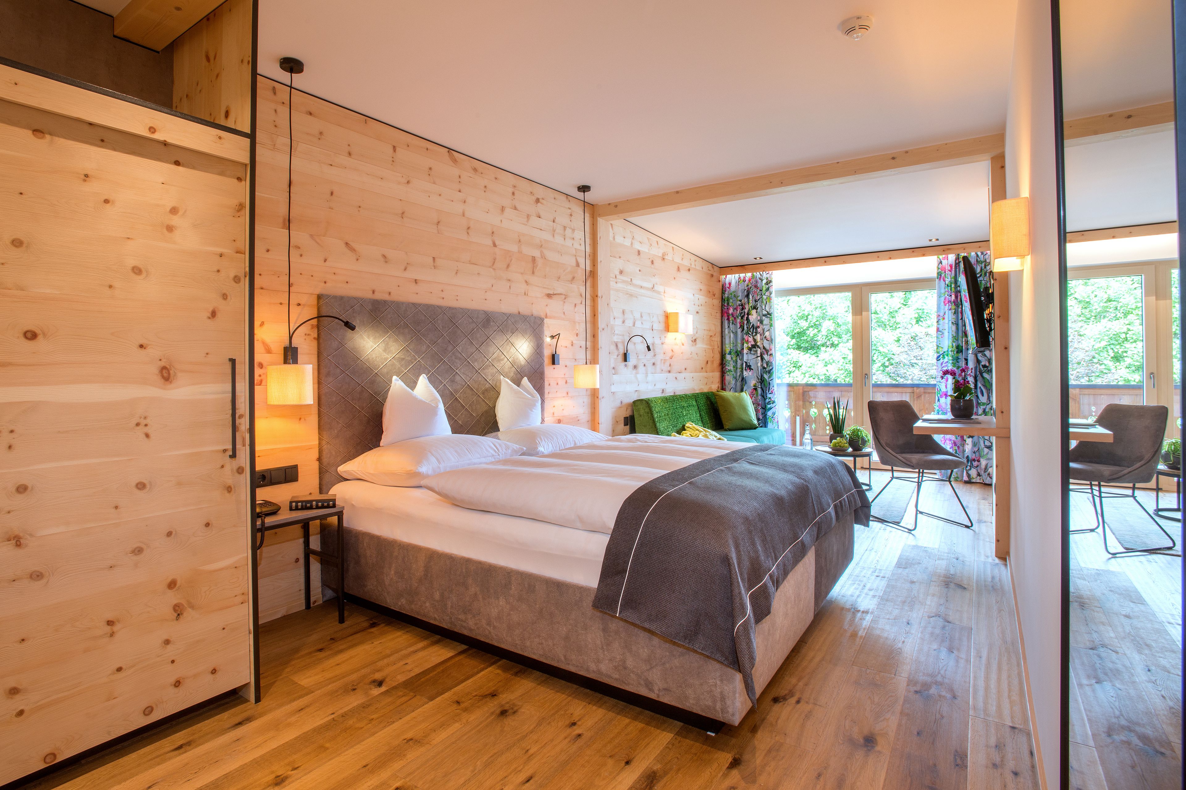 A modern bedroom with a large bed, wooden walls, and a balcony with seating.