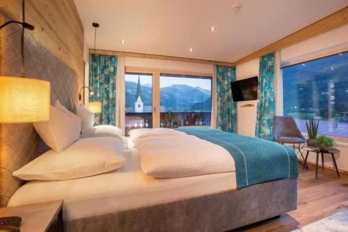 A modern hotel room with a large bed, a TV, and a view of mountains.