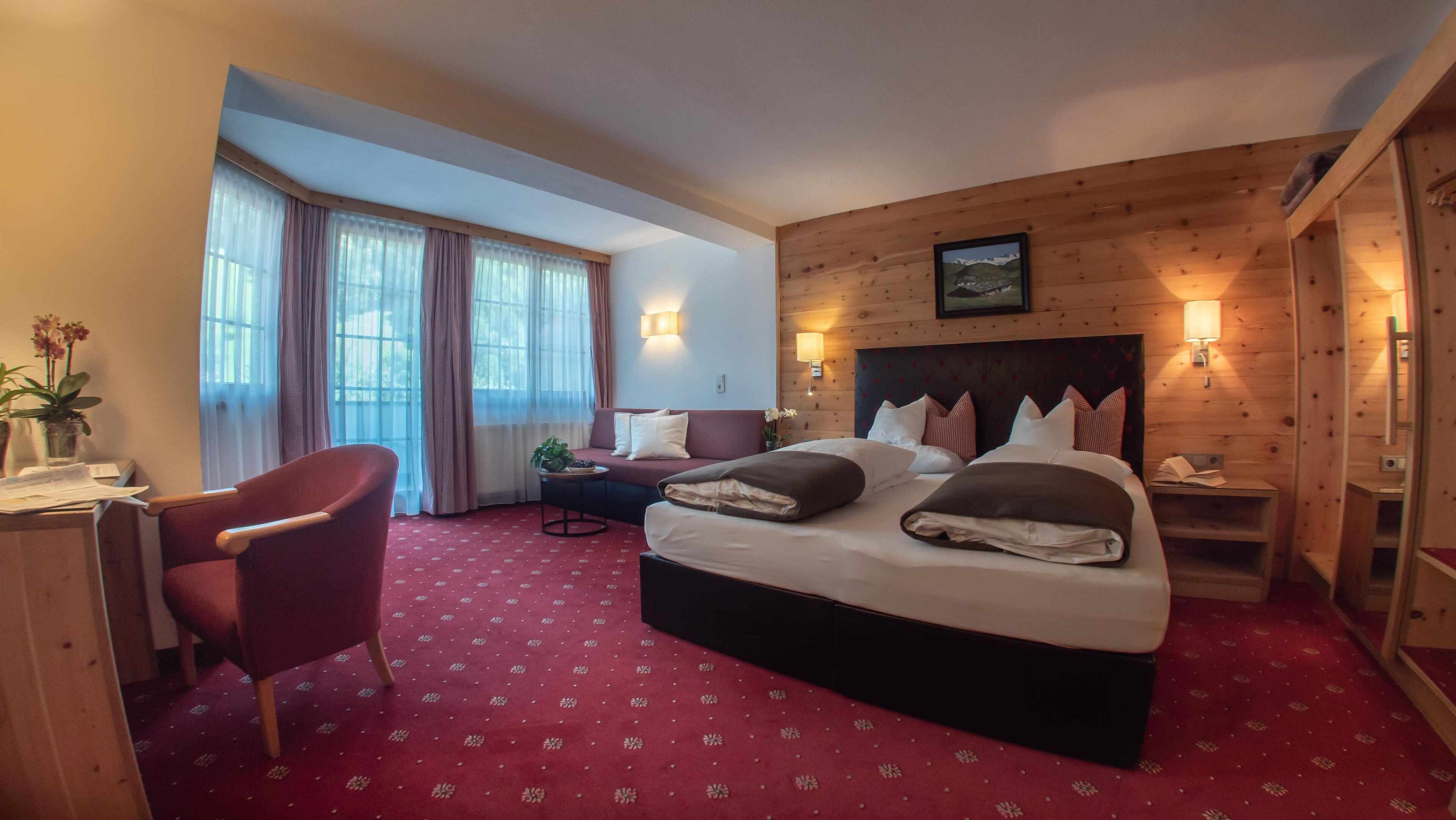 A hotel room with a large bed, a desk, a chair, and a window with curtains.
