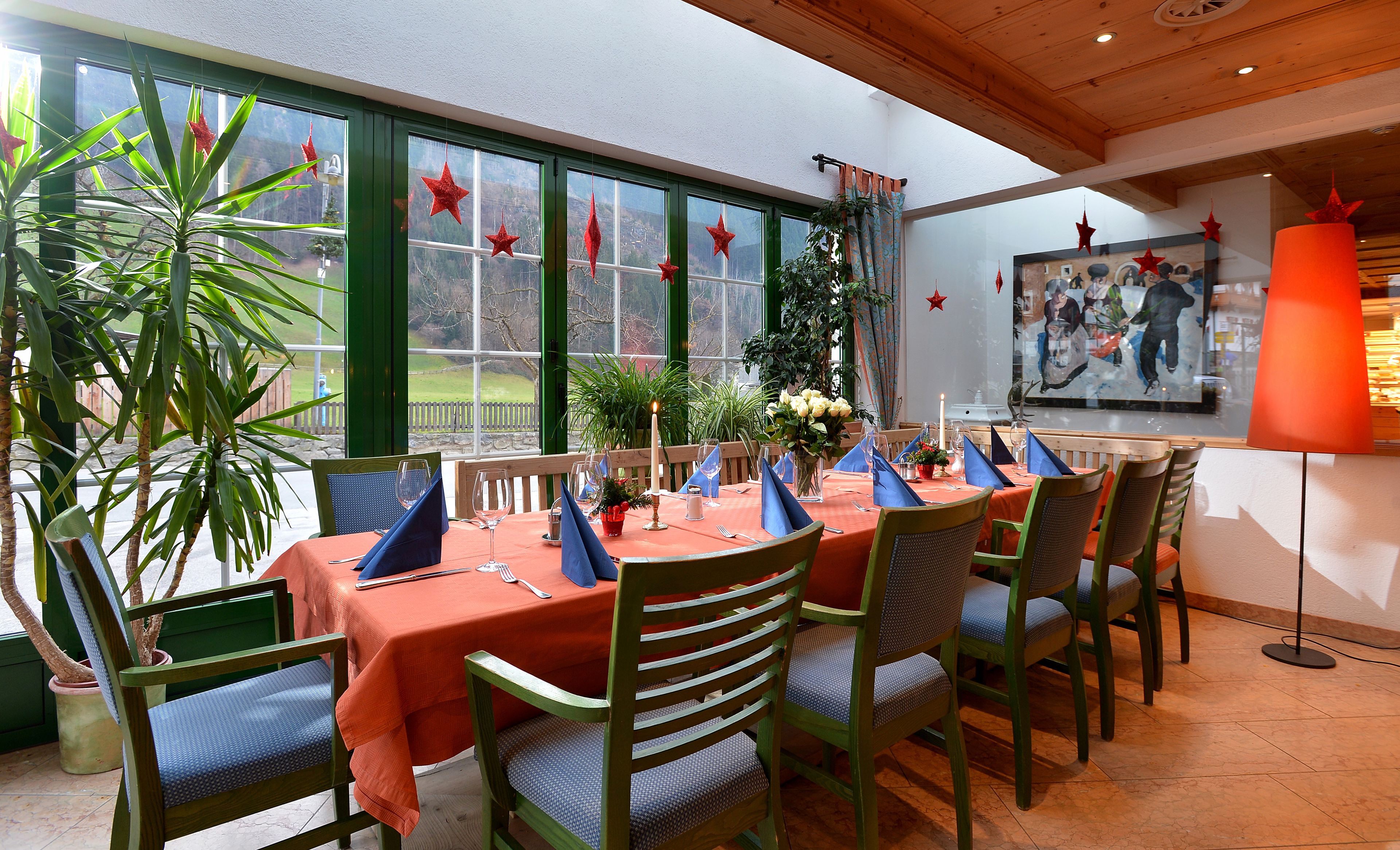 A dining area with a table set for six, surrounded by chairs, large windows, and indoor plants.