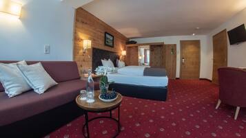 Habitación de hotel con pared de madera, una cama, un sofá, una mesita con un jarrón de flores y una alfombra roja.