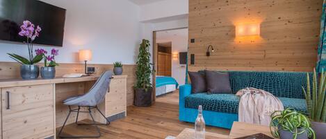 A modern living room with a wooden desk, a blue sofa, and a TV mounted on the wall.