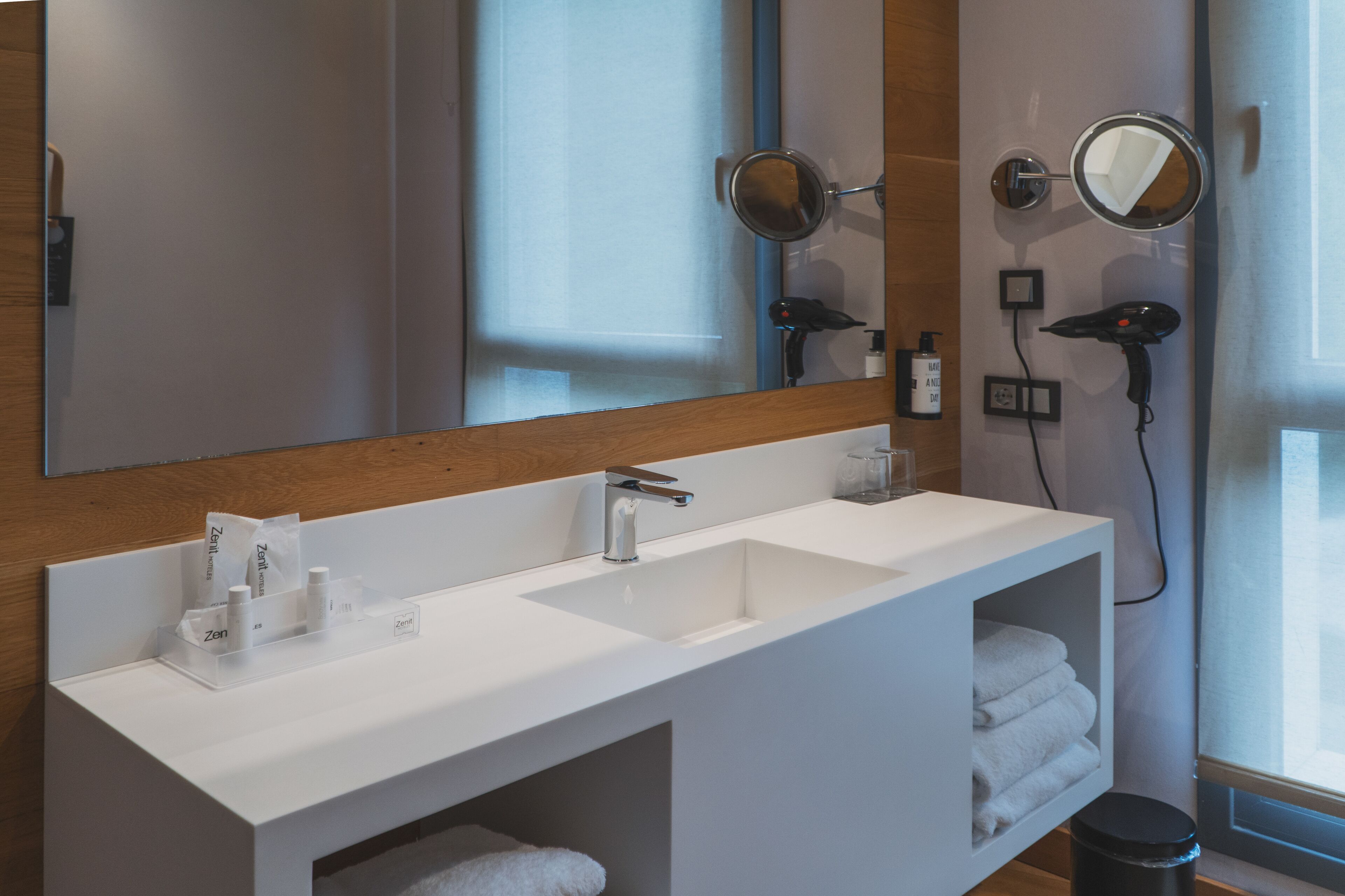 A modern bathroom with a white vanity, two sinks, a large mirror, and a hairdryer mounted on the wall.